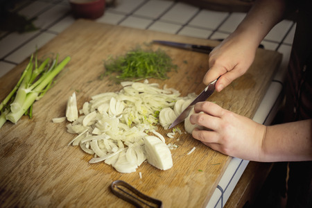 Close up view of a woman chopping fennel on a cutting board in a kitchenの写真素材