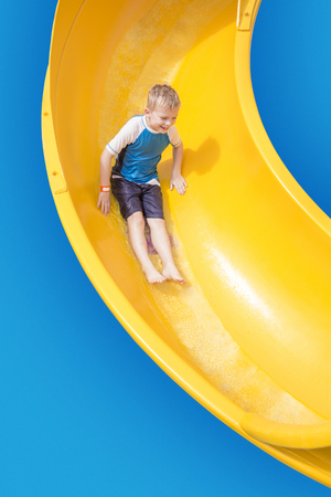 Smiling Young boy riding down a yellow water slideの写真素材