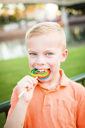 Cute young boy licking a large colorful lollipop outdoorsの写真素材