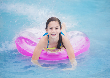 Cute girl smiling and having fun playing in the swimming pool during summer. Happy9 year old girl with braces and an adorable smile sitting on an inflatable floating tubeの写真素材