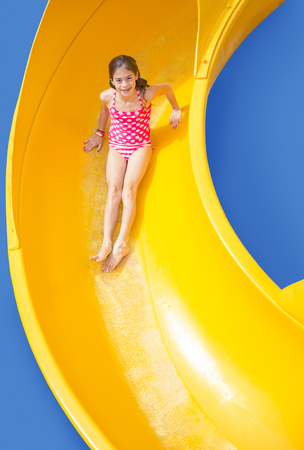 Smiling Young girl riding down a yellow water slideの写真素材
