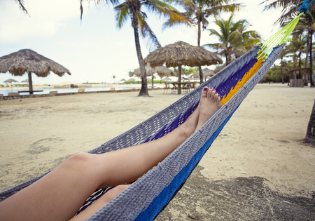 Beautiful female feet and legs relaxing in a blue hammock on the beach.の写真素材