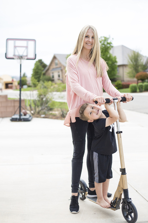 Cute young mother and her little boy playing together on a scooter in the driveway in a suburban neighborhood.の写真素材