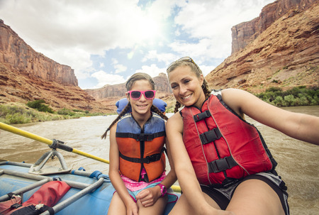 Active young family enjoying a day rafting down a whitewater river together. The mother and daughter sitting together on a large raft floating down a red rock canyonの写真素材