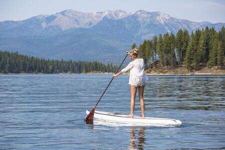 Beautiful woman paddle boarding on scenic mountain lakeの写真素材