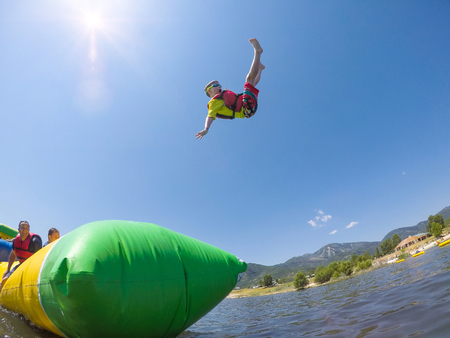 Young boy being launched in the air by in inflatable water toy at the lake on a warm summer day. He...