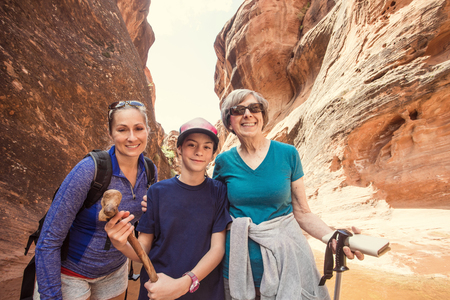 Three happy people hiking together in a red rock sandstone slot canyon in the deserts of Utah on an adventure vacation. Two women and a girl smiling and posing together during a fun hikeの写真素材