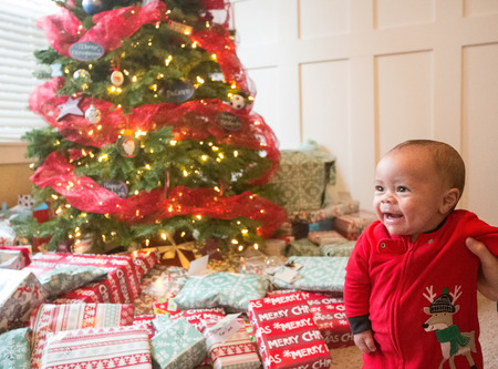 Cute diverse little boy smiling on Christmas morning in front of a Christmas tree surrounded by wrapped presentsの写真素材