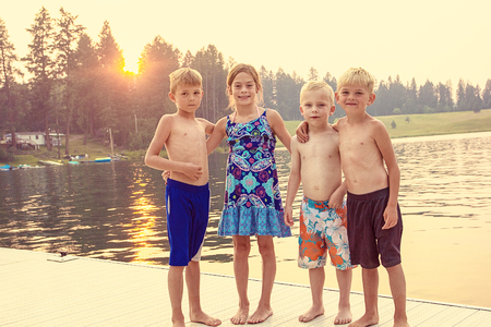 Four cute kids enjoying their summer vacation together at the lake. Playing together on the dock at sunset on a warm eveningの写真素材