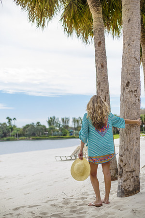 Beautiful woman in sundress walking on a tropical beach. View from behind of a gorgeous female enjoying a beautiful day at a tropical beach resortの写真素材
