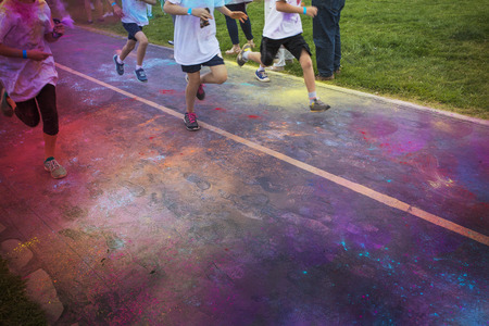 Abstract photo of a group of runners running in a color run race event. No faces visible on the legs and the feet and shoes of the runner. Lots of colorful clouds of chalk in the air and on the streetの写真素材
