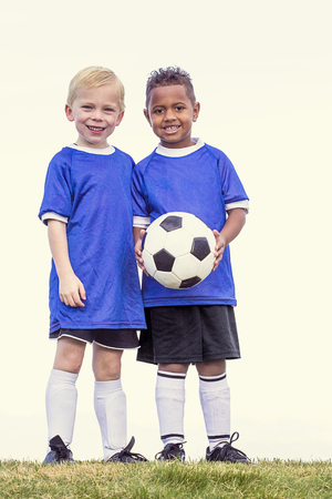 Full length view of two youth recreation league soccer players. Two diverse little boys standing on a grass fieldの写真素材