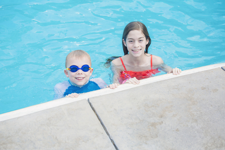 Two cute kids playing in a swimming pool on a sunny day while on vacation. Bright colorful fun summer photo with copy spaceの写真素材