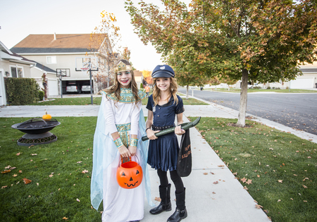 Group of kids dressed in Halloween costumes going trick or treating outdoors in October in a decorated neighborhoodの写真素材