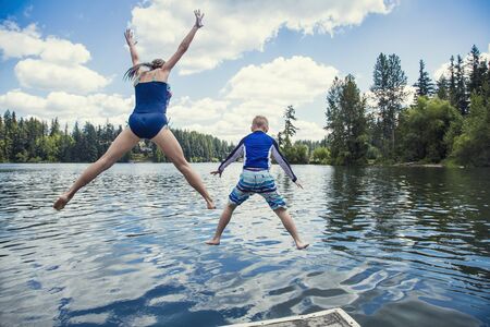 boy and girl jumping off the dock into a beautiful mountain lake. Having fun on a summer vacation. View from behindの写真素材