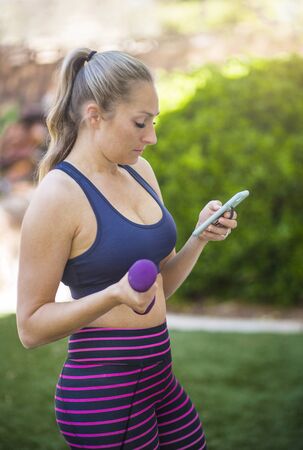 Candid photo of a beautiful fit middle aged woman doing a workout while looking at her cell phone.の写真素材
