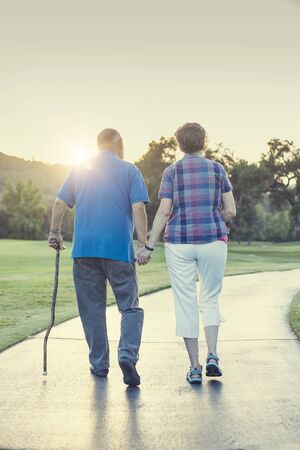 Senior couple holding hands and walking together outdoors on a sunny dayの写真素材