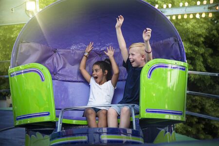 Two screaming Kids enjoying a fun summer amusement park ride. Arms raised and laughing as they twirl aroundの写真素材
