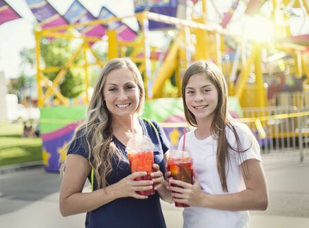 Two happy girls drinking a sweet beverage at an amusement park or summer carnival. Enjoying a cool drink on a warm summer eveningの写真素材