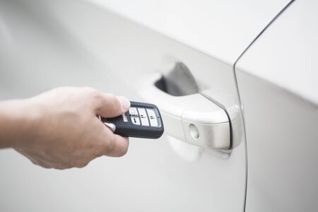 Human hand holding a keyless entry device or key fob to open the new car and start the car. focus on the keyless device system and door handleの写真素材