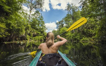 Adventuresome Woman kayaking along a beautiful tropical jungle river. Paddling along a calm beautiful river in a scenic natural backdropの写真素材