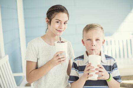 Two Cute kids drinking milkshakes or flavored drinks together outdoors on a warm summer day. Enjoying some cool liquid refreshmentの写真素材