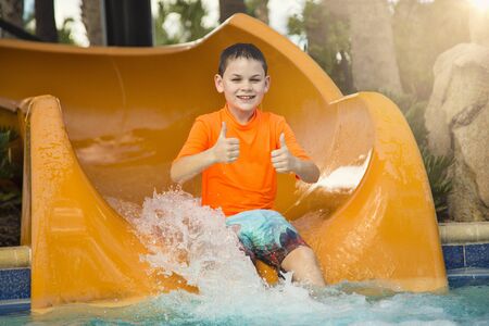 Cute happy boy riding down a water slide at an outdoor waterpark. Giving the thumbs up to show how he is having fun.の写真素材