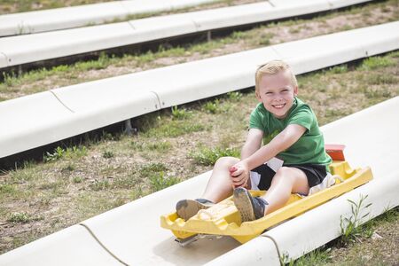 Cute smiling young boy riding downhill on an alpine coaster ride outdoors on a summers day. Happy and having fun on a thrilling theme park rideの写真素材