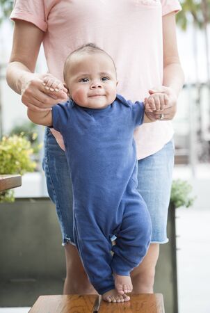 Adorable bi-racial baby boy learning to walk with the help of his mother. This happy cute child is learning how to move on his own for the first time. Taking His first steps forwardの写真素材