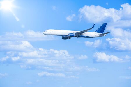 Large jet airplane flying in the sky full of clouds with the bright sun in the distanceの写真素材