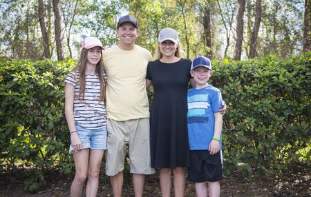 Cute young family portrait all wearing baseball hats outdoors. Smiling and showing off their different caps they have on their headsの写真素材