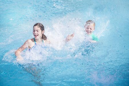 Two cute kids laughing and splashing each other in the swimming pool while on a summer vacation . Water is splashing everywhere and kids are having lots of funの写真素材