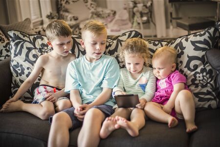 Group of kids sitting together playing with an electronic tablet devicesの写真素材