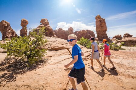 Happy family hiking together in the beautiful rock formations of Arches National Park. Walking along a scenic trail with large rock unique formations in the backgroundの写真素材