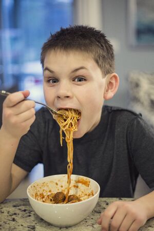 Hungry and Excited boy taking a huge bite of spaghettiの写真素材
