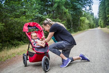 Woman and her little boy taking a break from working out. Playing together and smiling together. Boy riding in a jogging stroller on a scenic running trailの写真素材