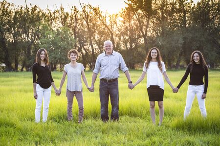 Attractive Smiling beautiful family holding hands together outdoors in a grass field. Happy family...