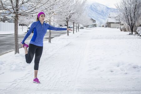 Attractive Woman jogging and stretching outdoors during winter weather and snow on the ground. Horizontal photo of a woman working out during the winter monthsの写真素材