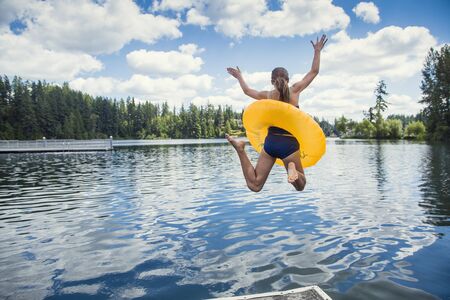 A little girl jumping off the dock into a beautiful mountain lake. Having fun on a summer vacationの写真素材