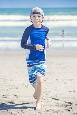 Active, Healthy Boy running on the beach on a sunny day in Florida. Smiling and enjoying nature on a sunny warm day. Exercising and being active during the summerの写真素材