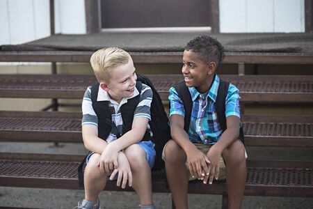 Candid photo of two students talking together at school. Smiling boys having fun together sitting on the stairs enjoying their friendshipの写真素材
