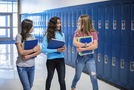 Candid photo of Three Junior High school Students talking together in a school hallway. Diverse Female school girls smiling and having fun together during a break at schoolの写真素材