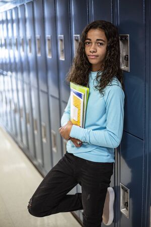 Portrait of a diverse Junior High school Student standing in a school hallway. Diverse school girl looking and holding her books during breaks in the dayの写真素材