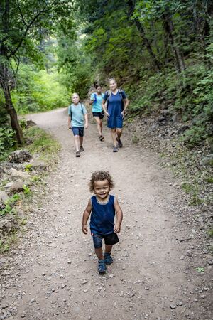 Family hiking together along a scenic mountain trail on a summer day. Selective focus Lifestyle photo of people outdoors enjoying nature and being activeの写真素材
