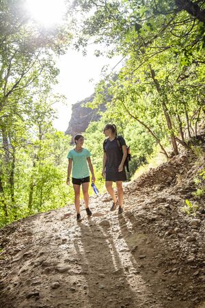 Two women hiking together along a scenic mountain trail on a summer day. Lifestyle photo of people outdoors enjoying nature and being activeの写真素材