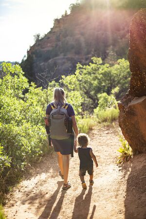 Mother and child hiking together along a scenic mountain trail on a summer day. Lifestyle photo of people outdoors enjoying nature and being activeの写真素材