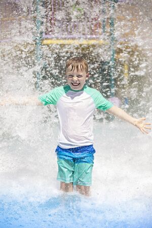 Young boy getting soaking wet while at an outdoor water park. Lots of water splashing water behind the boy. He is smiling and anticipating getting wet and drenchedの写真素材