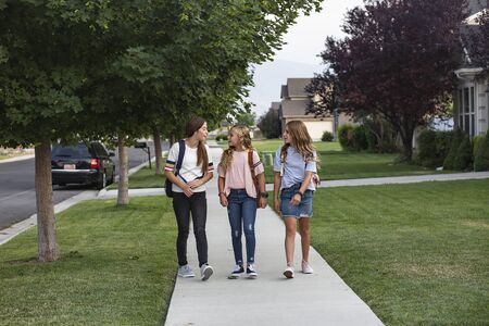 Group of cute young female friends and students talking together as they walk home school for the dayの写真素材