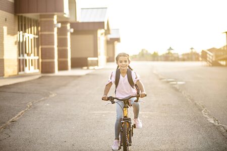 Diverse Young girl riding her bicycle home from school. Education concept photo of diversity in schoolの写真素材