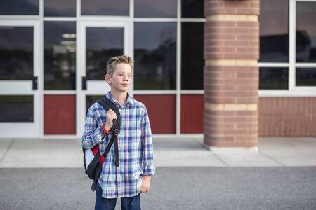 Candid portrait of a male elementary school student standing outside the school building. Handsome boy with his backpack heading home from school at the end of the dayの写真素材